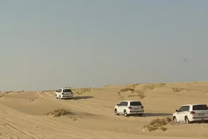 SUVs navigating through golden desert dunes on an exhilarating safari adventure under clear blue skies.