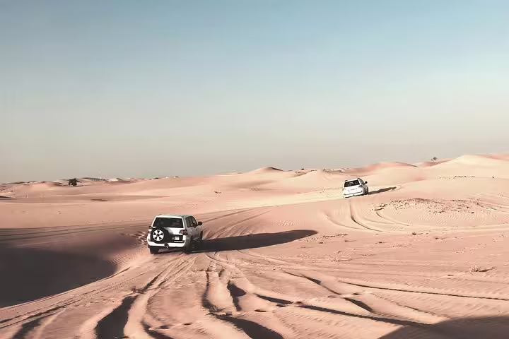 SUVs navigate the expansive sand dunes under a clear sky on a thrilling desert safari in Qatar.