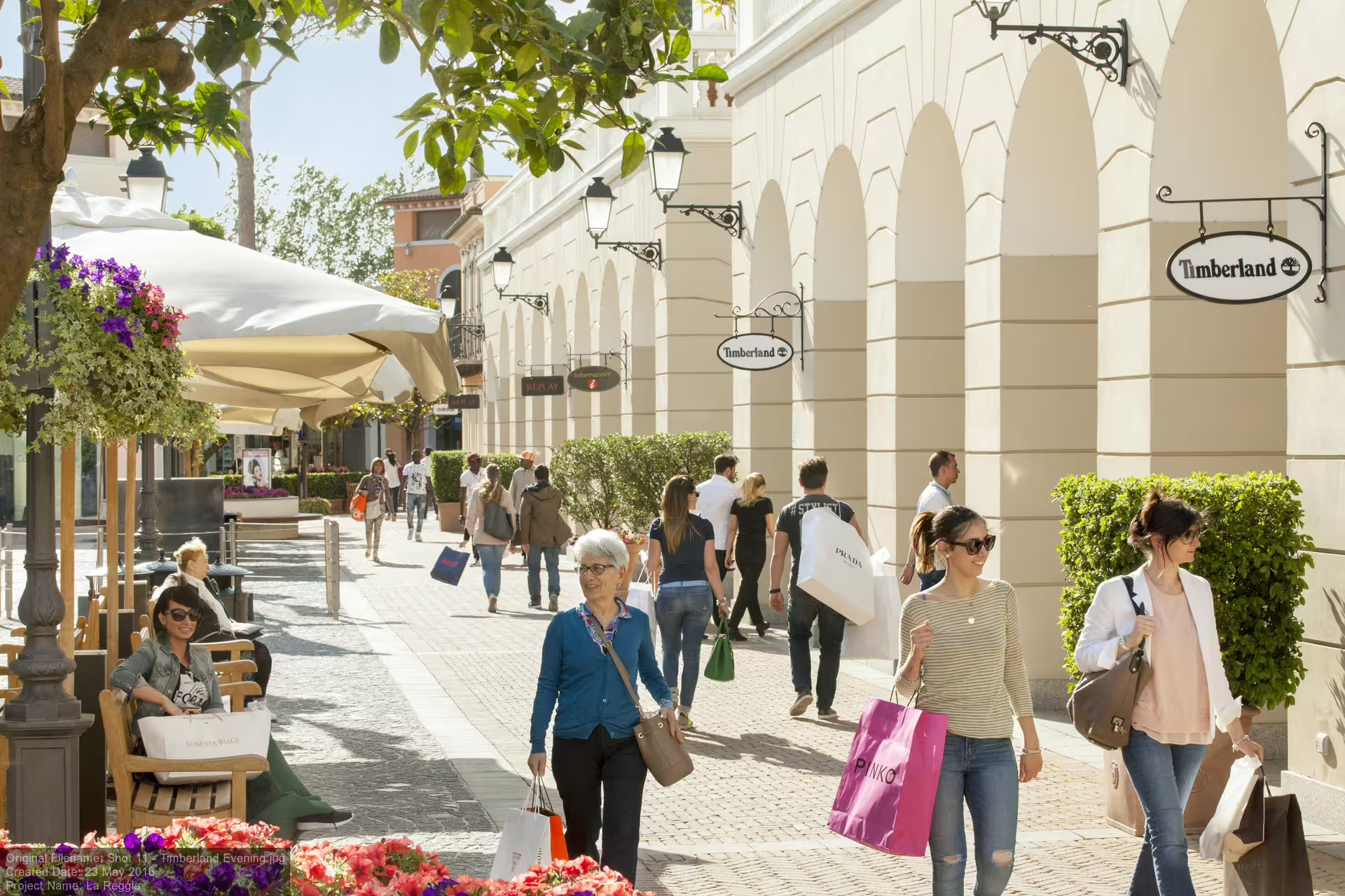 Visitors stroll with branded bags along the sunny, tree-lined streets of Designer Outlet La Reggia near Naples, Italy