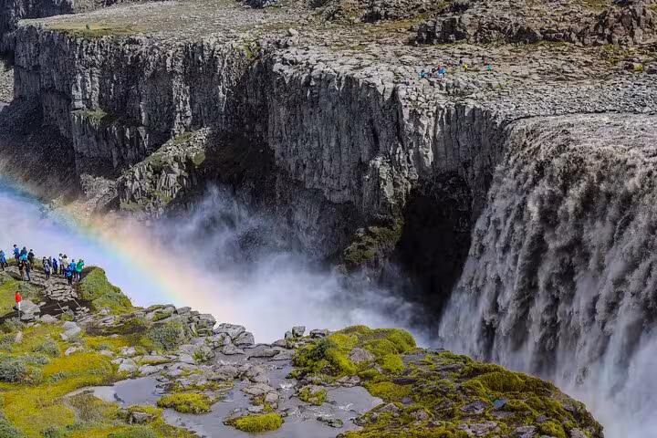 Tourists admire Dettifoss waterfall's powerful cascade and rainbow in Iceland's rugged landscape.