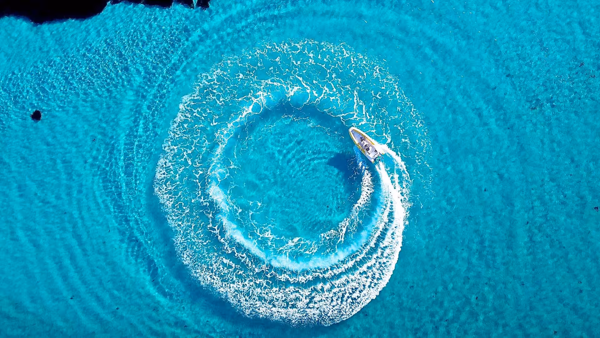 Aerial view of a dinghy creating a circular wake in the vibrant turquoise waters near Asinara Island, perfect for a thrilling tour.