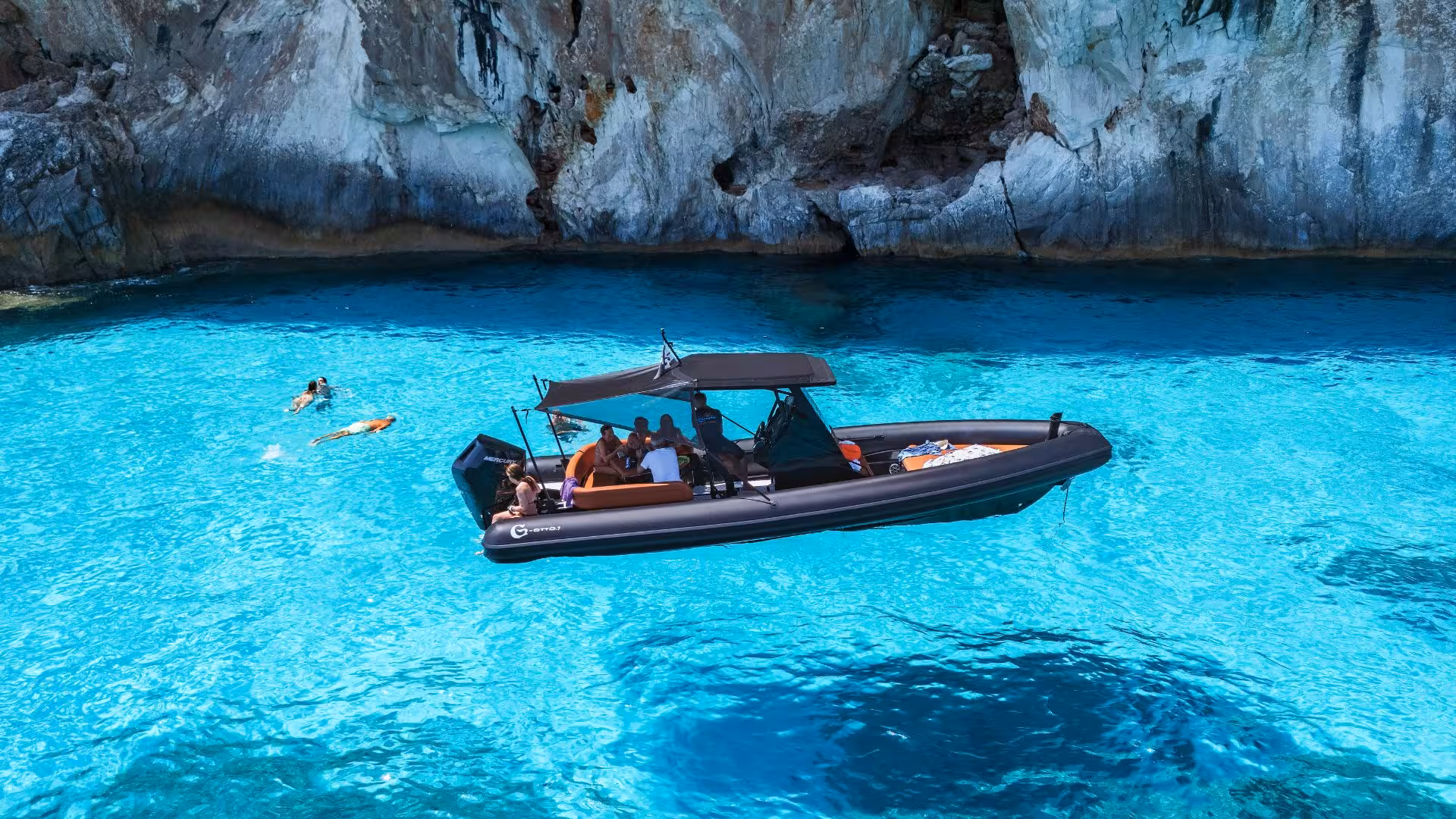 Tourists enjoy a dinghy ride on crystal-clear waters near Cala Goloritzè, surrounded by stunning cliffs.