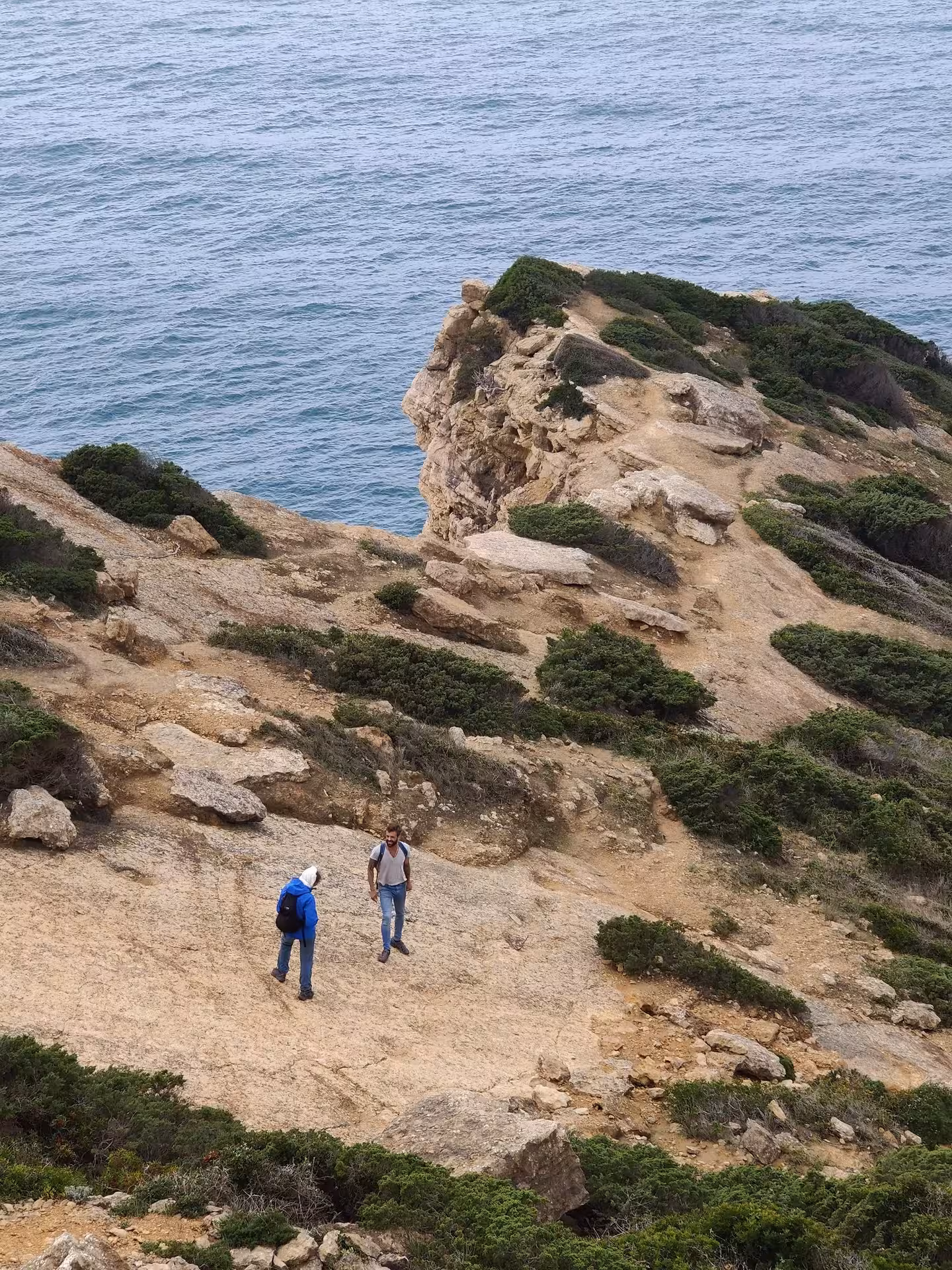 Hikers crossing rocky coastal trail above the Atlantic near Cabo Espichel on the dinosaur footprints hike