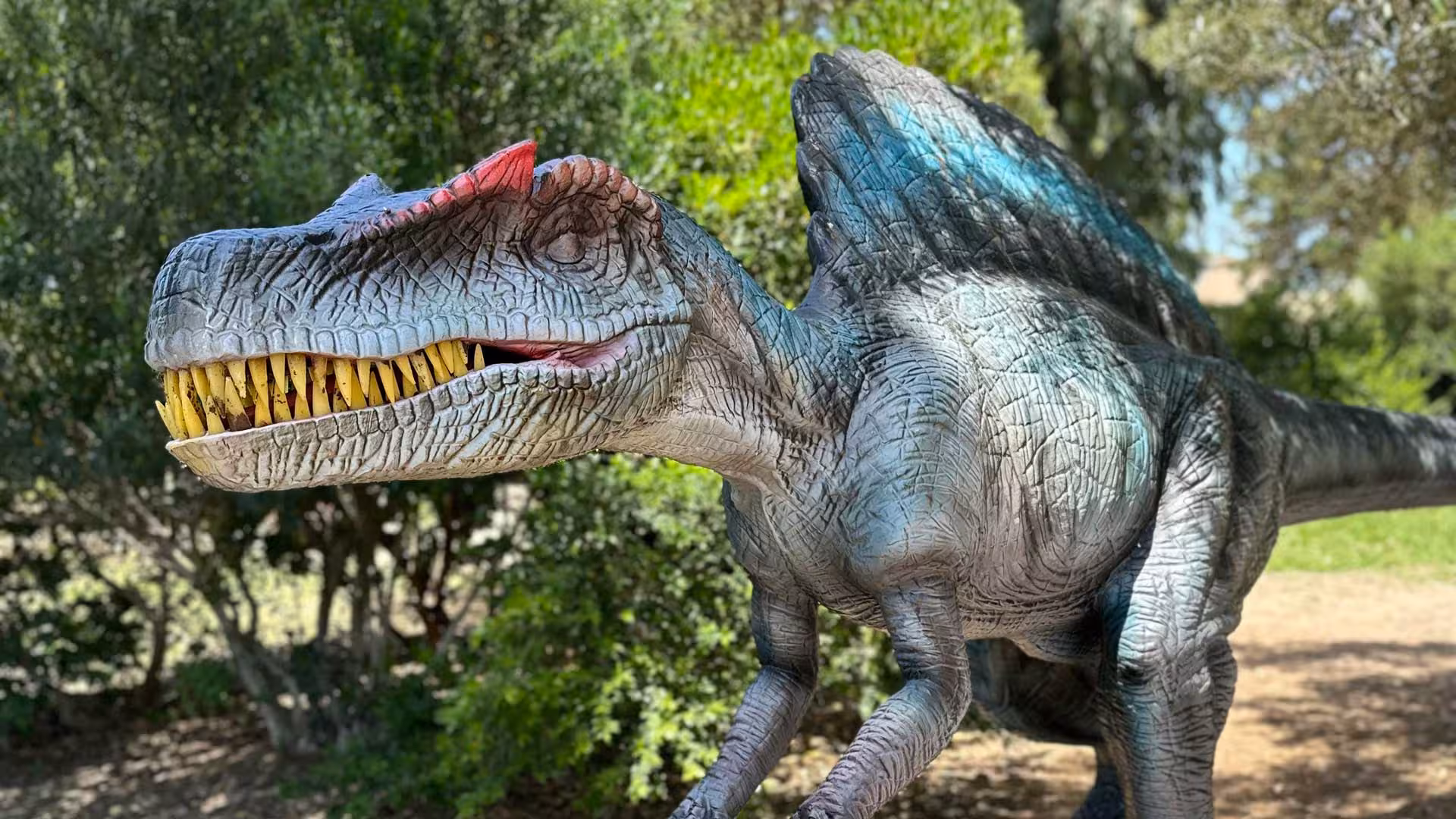 Close-up of a dinosaur model in Porto Conte Park, Alghero, with striking teeth and natural green surroundings.