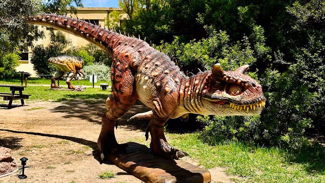 Lifelike dinosaur sculpture amidst lush greenery at Porto Conte Park, Alghero, ideal for family-friendly tours.