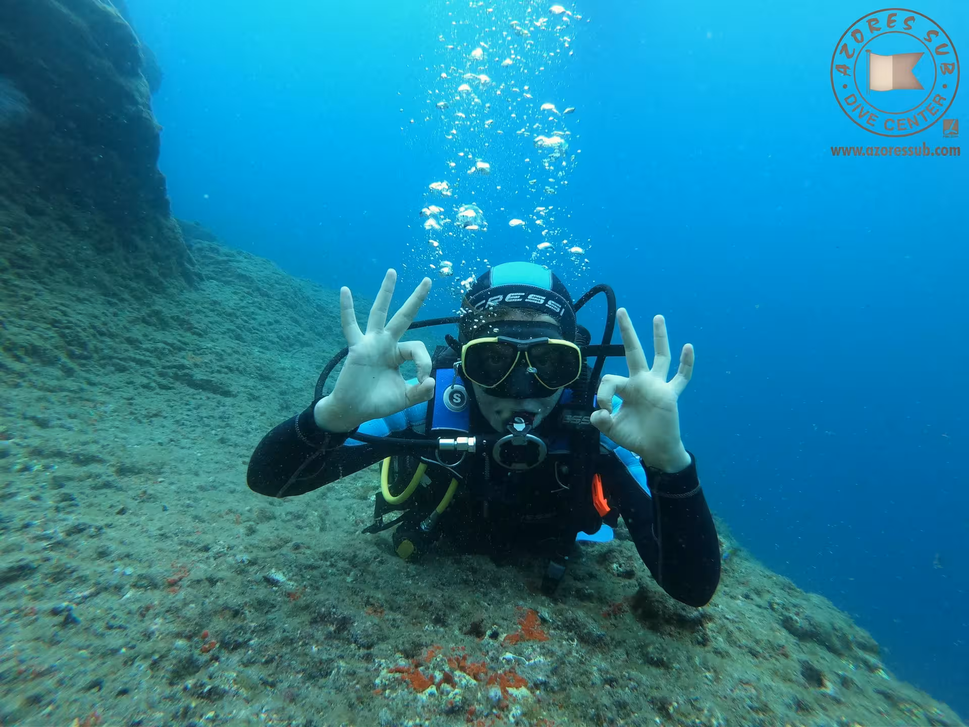 Diver giving OK sign underwater in clear sea, showcasing a pool and sea baptism tour with safe guided experience
