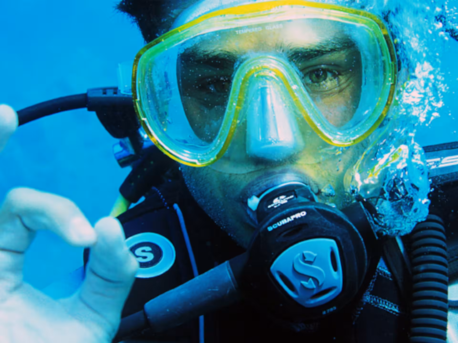 Close-up of a diver underwater at Ruja Island, showcasing diving gear and making an okay sign during sea baptism.