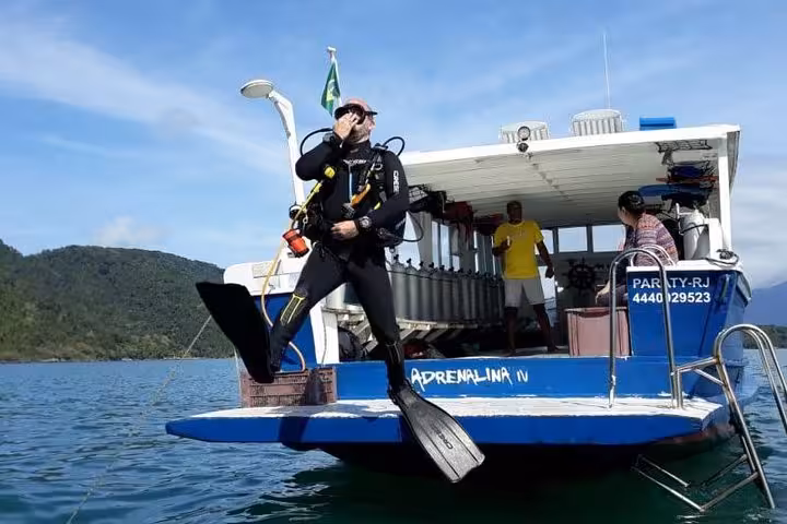 Diver prepares to enter the clear waters from a boat during the Diving Baptism tour near lush Brazilian coastline.