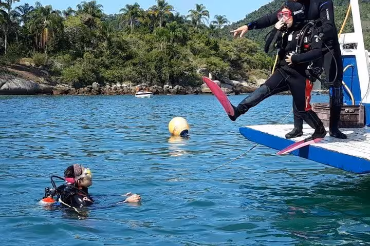 A diver makes a splash entering the water from a boat on a scenic diving baptism tour with lush greenery in the background.