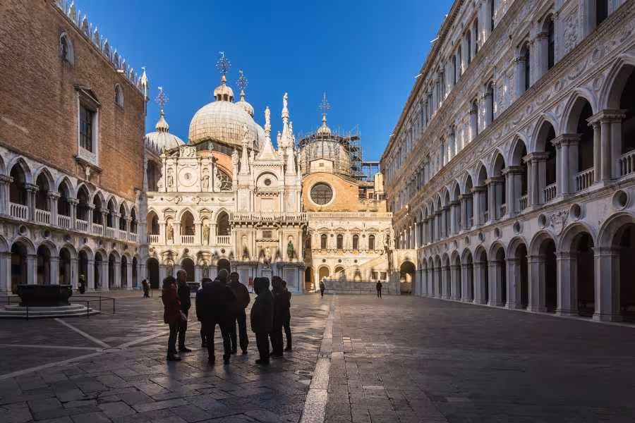 Visitors admire the stunning architecture of the Doge’s Palace courtyard, featuring domes and gothic arches.