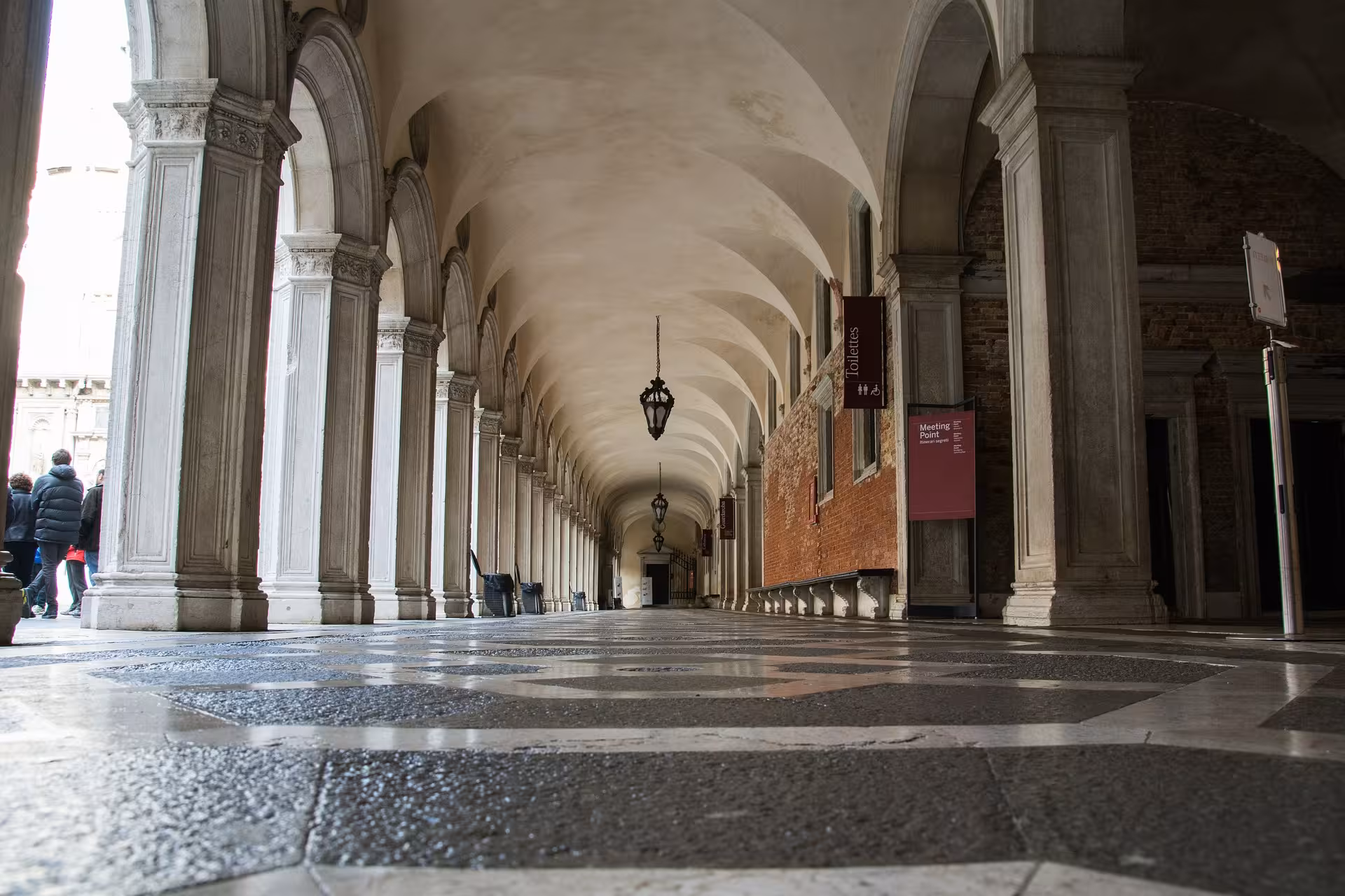 Elegant arched corridor with detailed columns and patterned floor at the Doge’s Palace in Venice.