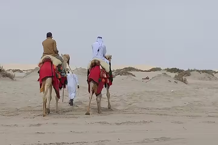Two riders on camels adorned in traditional attire traversing the serene desert landscape near Doha.