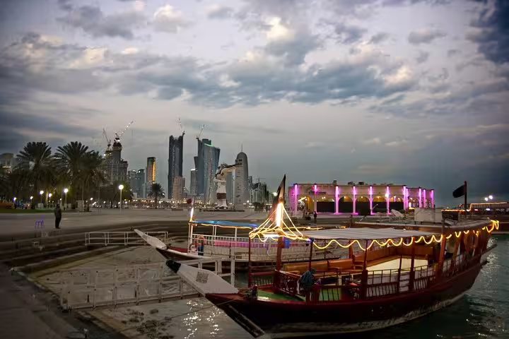 Traditional dhow boat illuminated at night with Doha skyline in the background on a city tour.