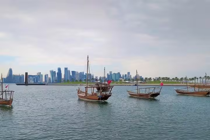 Traditional wooden dhows sail against Doha's modern skyline, perfect for a customized private city tour experience.