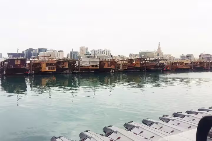 Traditional wooden dhows lined up at Doha's waterfront with the cityscape in the background, showcasing Qatar's rich maritime history.
