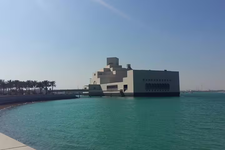 The iconic Museum of Islamic Art in Doha, Qatar, set against a clear blue sky and turquoise waterfront.