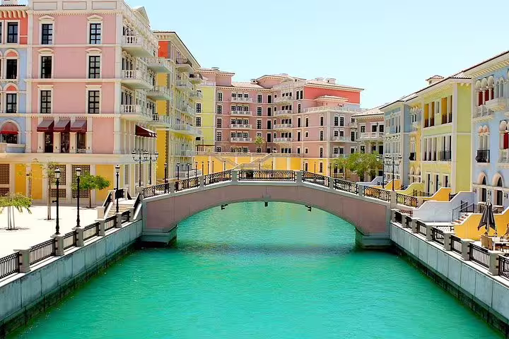 Charming canal view in The Pearl, Doha, featuring colorful Mediterranean-style buildings and a picturesque bridge.