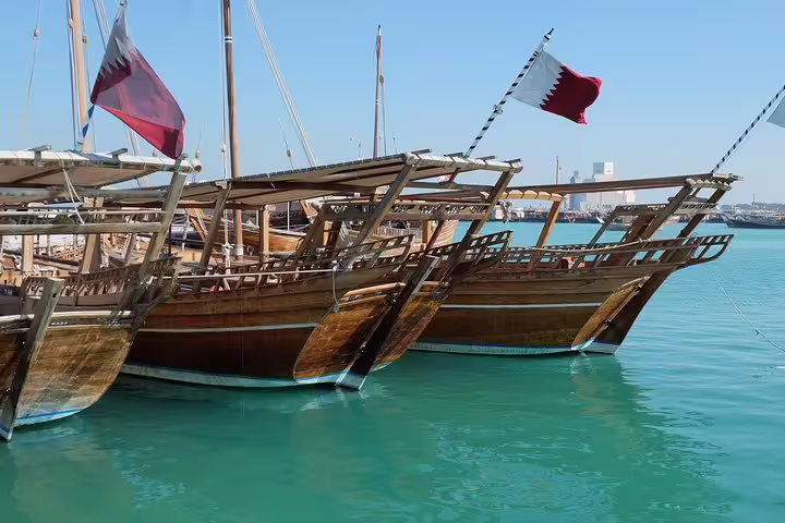 Traditional wooden dhows with Qatari flags docked in the clear waters of Doha's harbor, perfect for a private city tour.