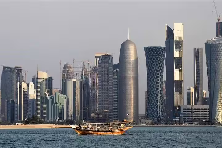 Scenic view of Doha's skyline with a traditional dhow boat on the Corniche waterfront, highlighting Qatar's urban beauty.