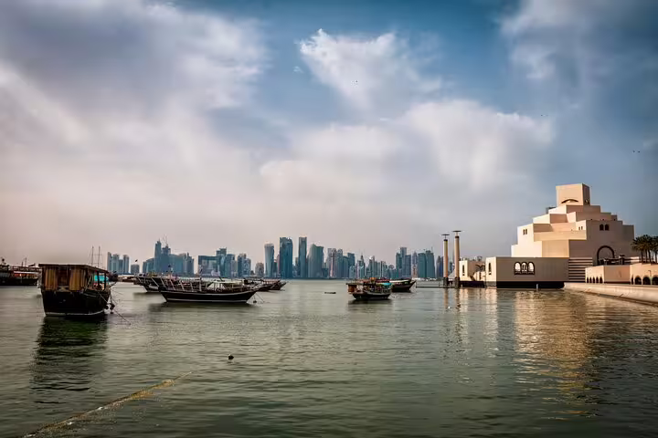 Scenic view of Doha skyline and traditional boats by the Museum of Islamic Art on a clear day during transit city tour.