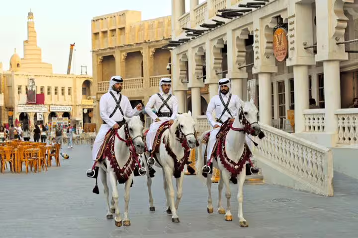 Three men in traditional attire riding horses at Souq Waqif, highlighting Doha's cultural heritage and vibrant atmosphere.