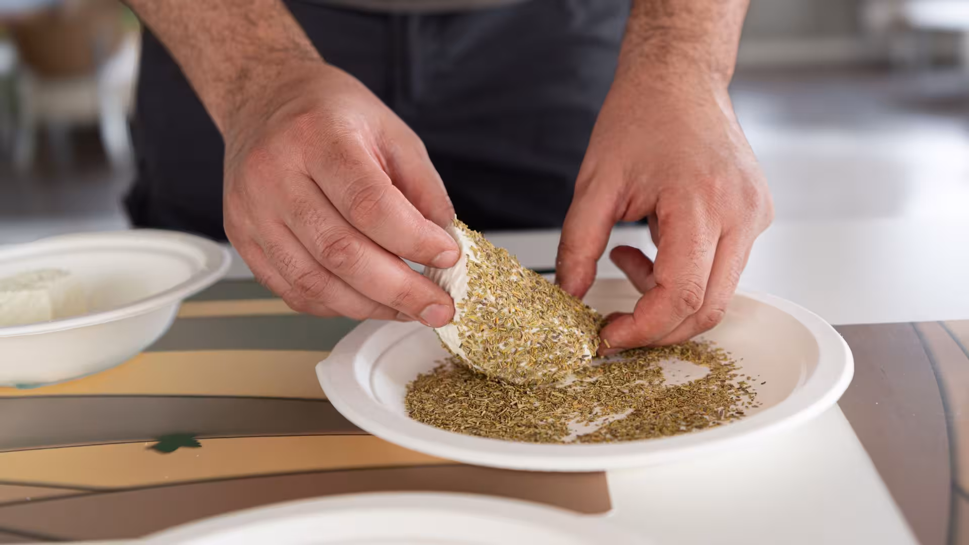 Hands rolling fresh cheese in aromatic herbs during Dolianova cheese factory workshop tour.