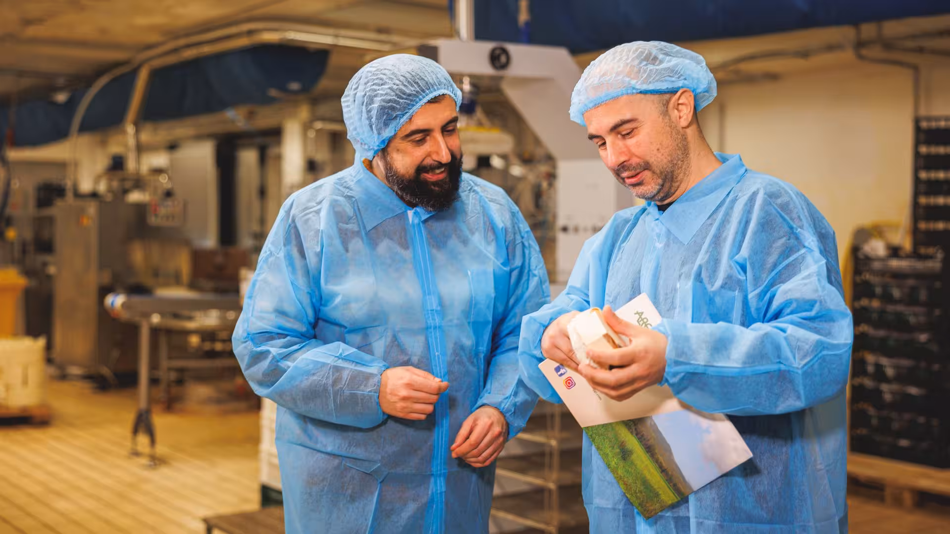 Two men in blue protective clothing examining cheese packaging at Dolianova cheese factory visit.