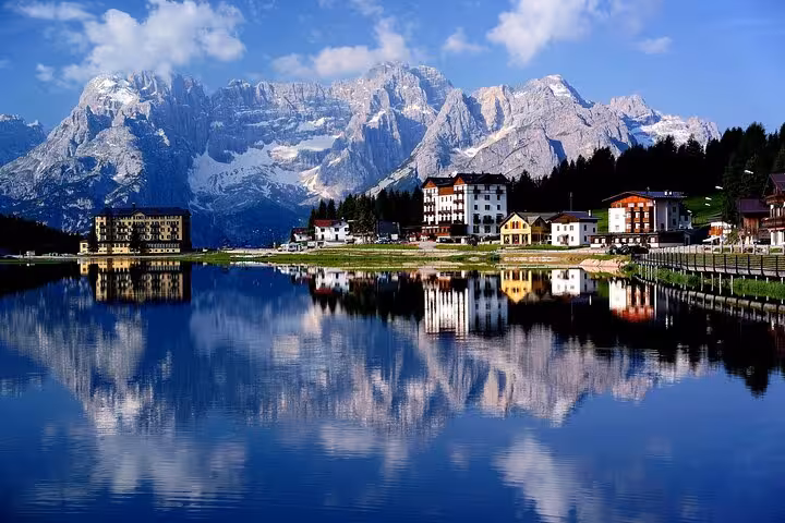 Picturesque Dolomites with vibrant alpine village reflecting in a serene lake under a brilliant blue sky.