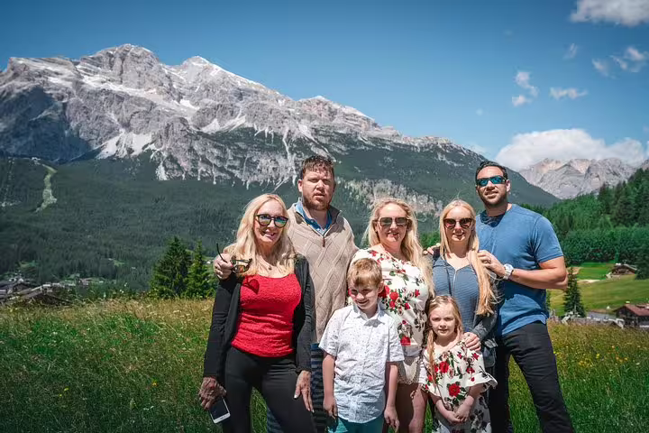 Family enjoying a sunny day in the Dolomites with majestic mountains and lush greenery around them.