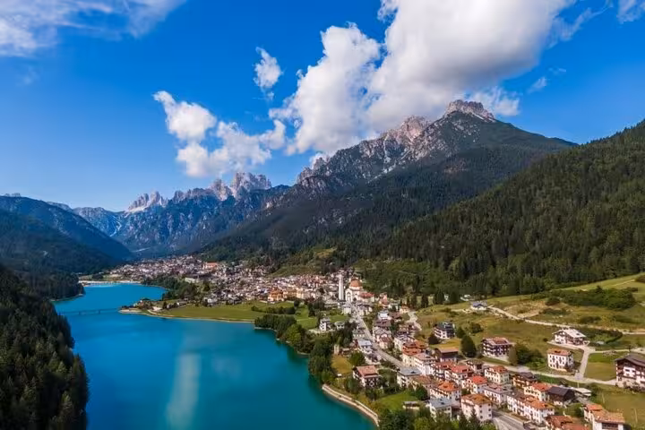 Aerial view of an Italian village nestled by turquoise lakes and majestic Dolomites, ideal for Venice day trips.