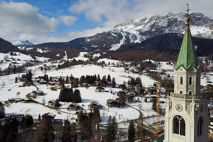 Scenic view of snowy Dolomites village with a green-spired church tower, perfect for a Venice day trip.