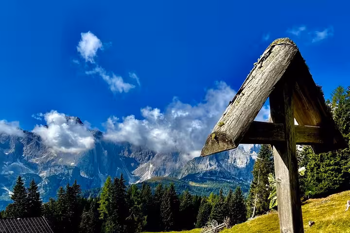 Scenic view of the Dolomites with a rustic wooden cross under clear blue skies, perfect for day tours from Venice.
