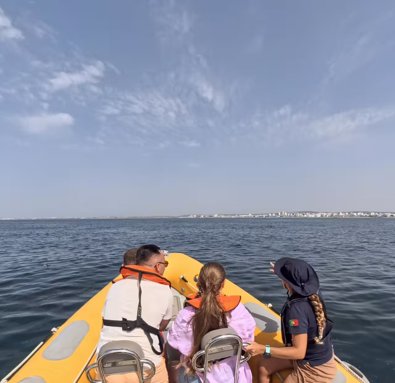 Guests in life jackets on a yellow RIB scan the horizon on a coastal wildlife watching dolphin tour