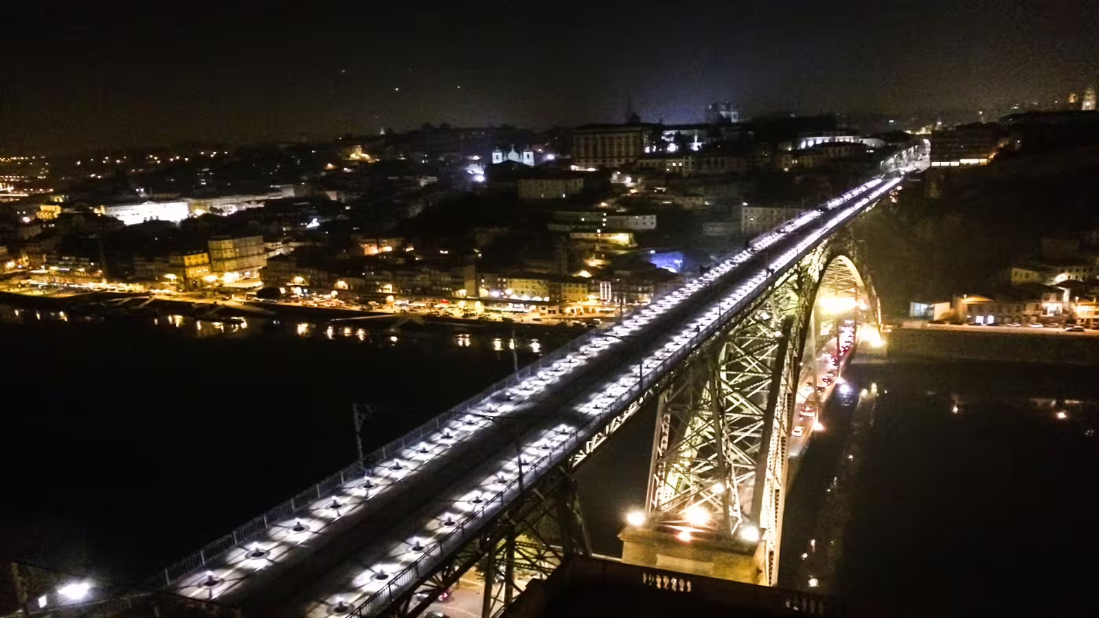 Illuminated Dom Luís I Bridge spanning the Douro River in Porto at night, showcasing the city's vibrant architecture and lights.