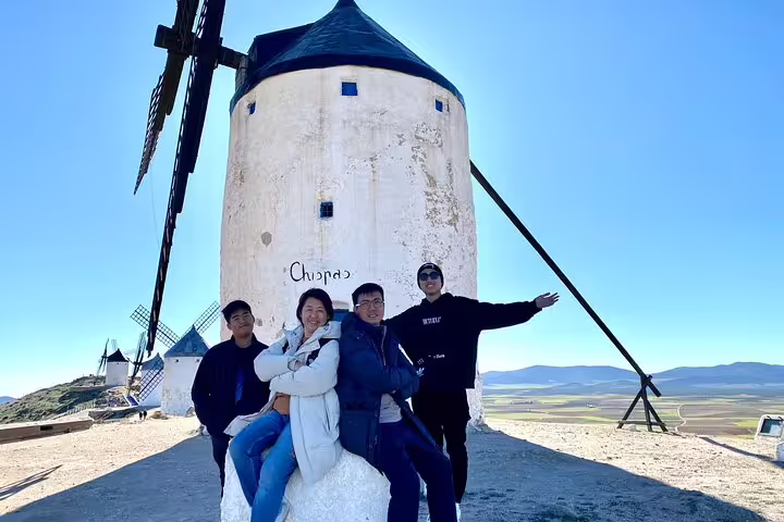 Friends smile near famous Don Quixote windmill on a sunny La Mancha cultural heritage tour.