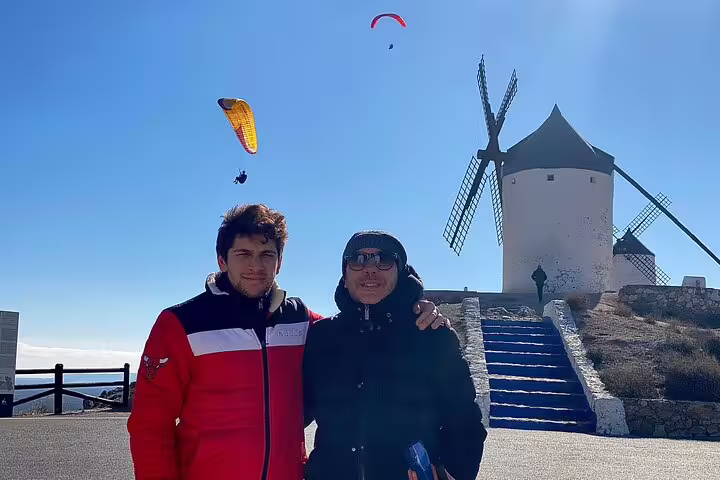 Visitors posing by iconic La Mancha windmills with paragliders in the sky on a Don Quixote adventure.