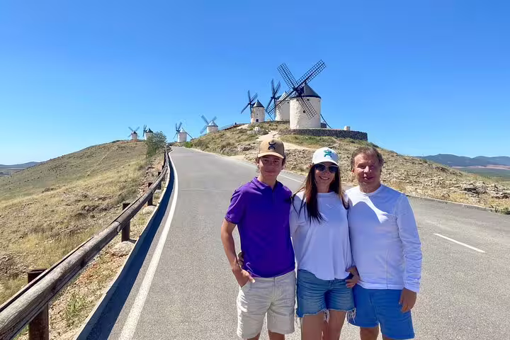 Family posing on a road leading to the picturesque Don Quixote windmills of La Mancha with clear skies above.