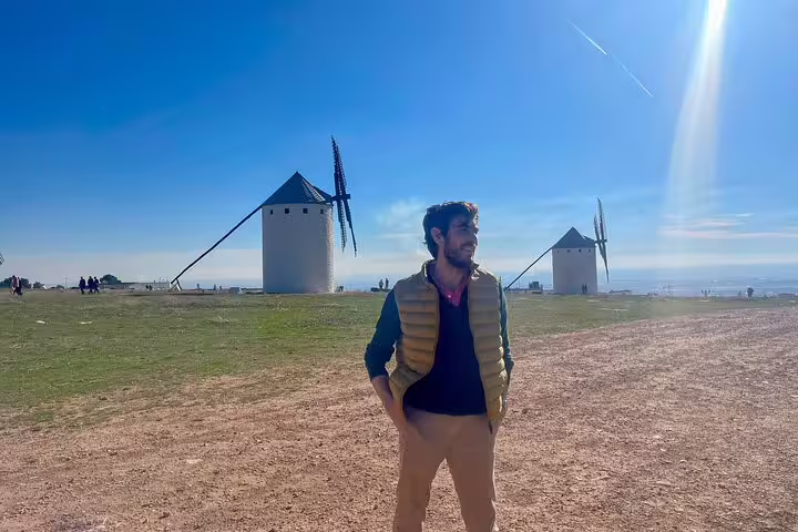 Tourist enjoying the scenic view of iconic Don Quixote windmills in La Mancha under a clear blue sky.
