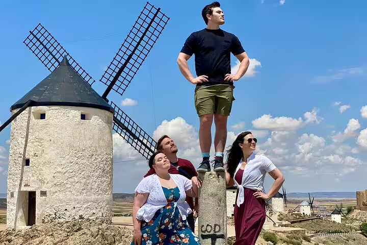 Visitors posing by iconic Don Quixote windmills in La Mancha under a vibrant blue sky, part of a cultural tour.
