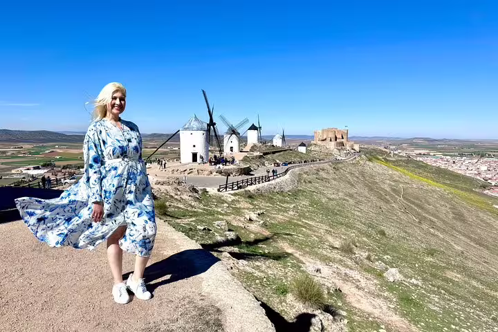 Visitor enjoys stunning view of iconic Don Quixote windmills in La Mancha under clear blue skies.