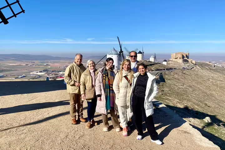 Tour group poses in front of historic windmills and castle on La Mancha's scenic landscape tour.