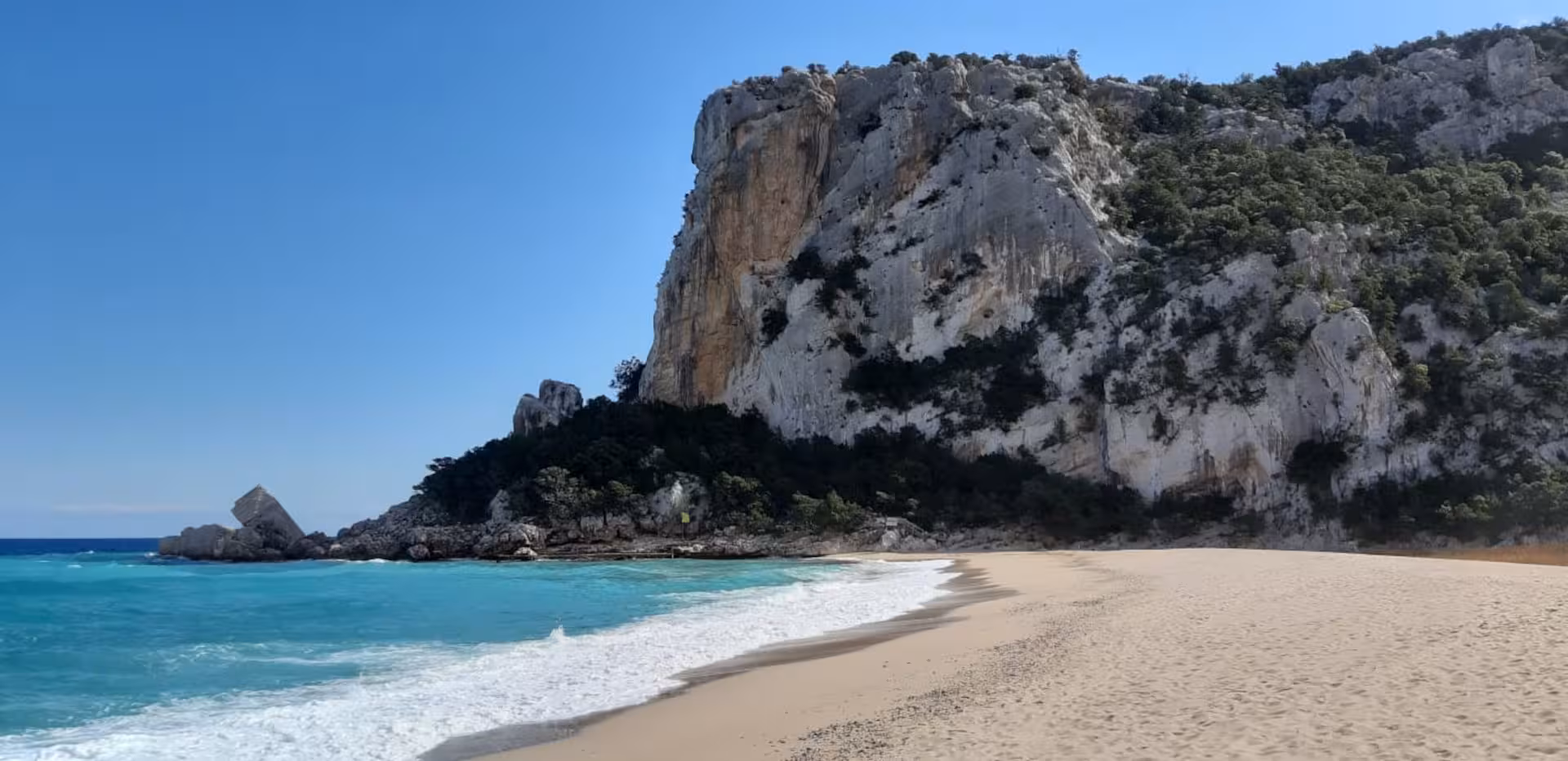 Cala Luna's pristine sandy beach with crystal-clear waters and striking limestone cliffs, perfect for trekking adventures.