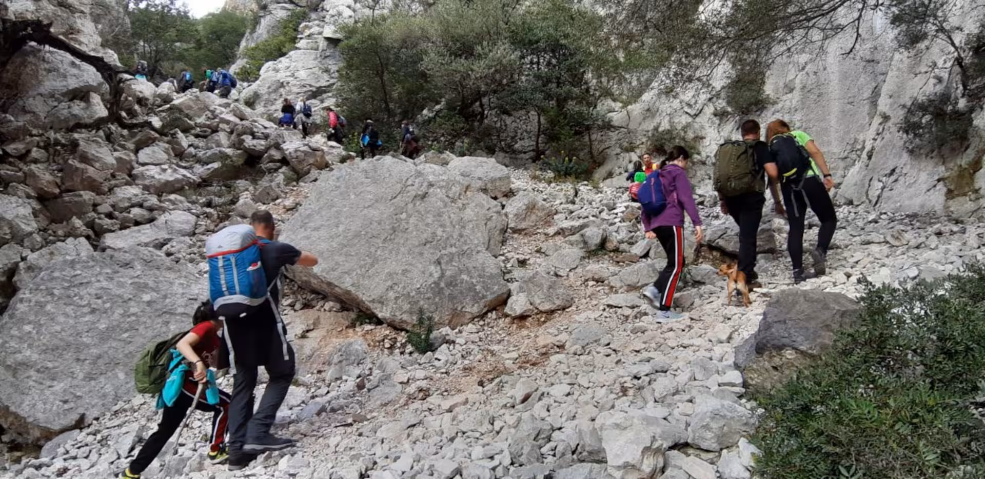 Group of hikers trekking through rocky terrain towards Cala Luna, showcasing challenging yet rewarding trails.