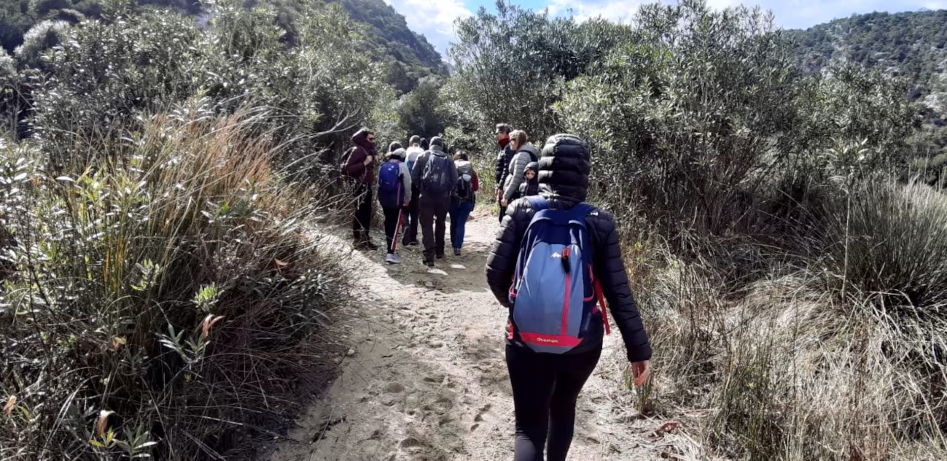 Group of hikers on a scenic trail surrounded by lush greenery near Dorgali, Sardinia, heading towards Cala Luna beach.
