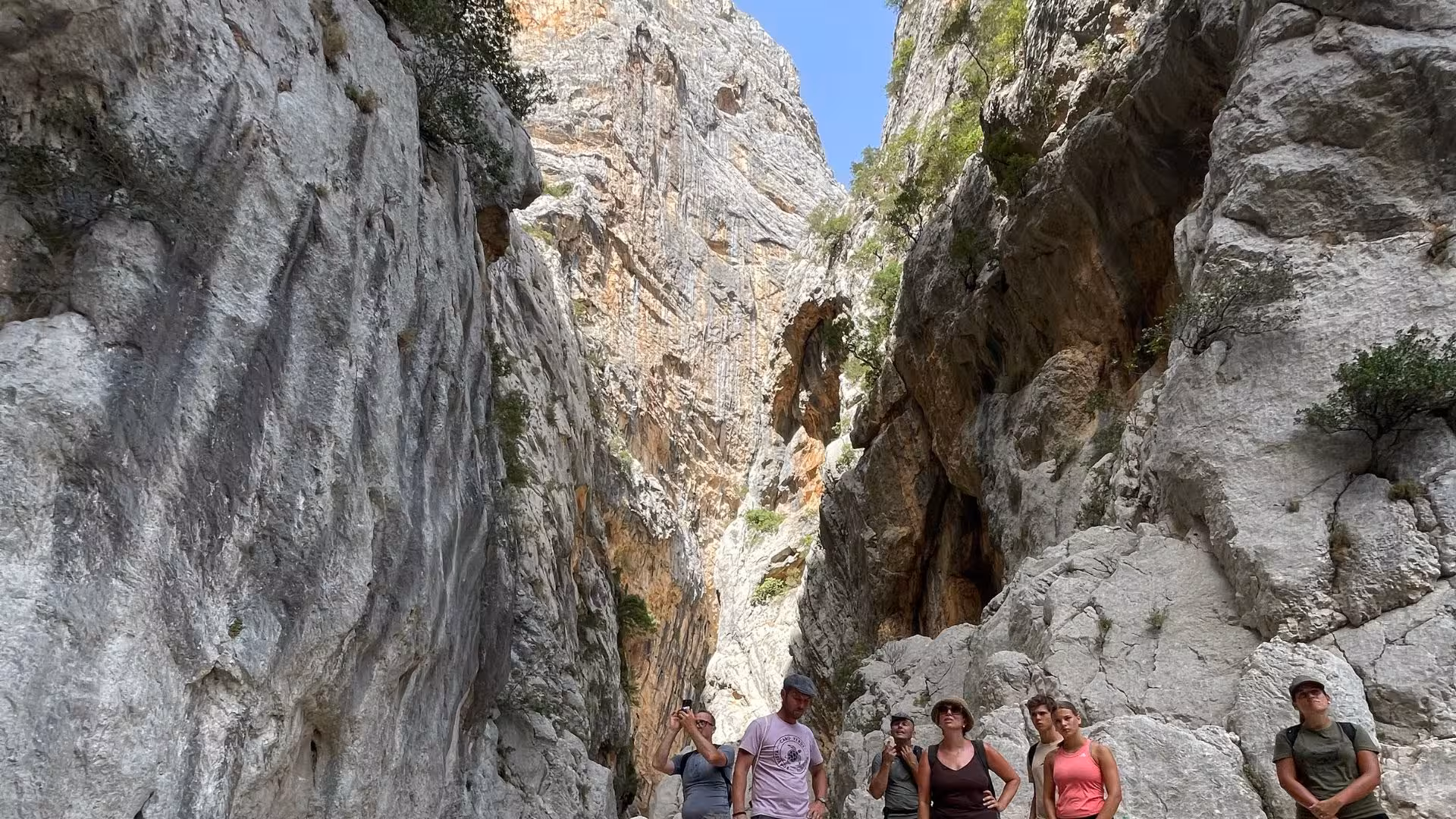 Hikers exploring the towering rock formations of Gorropu Canyon on a clear day from the Dorgali trekking tour.
