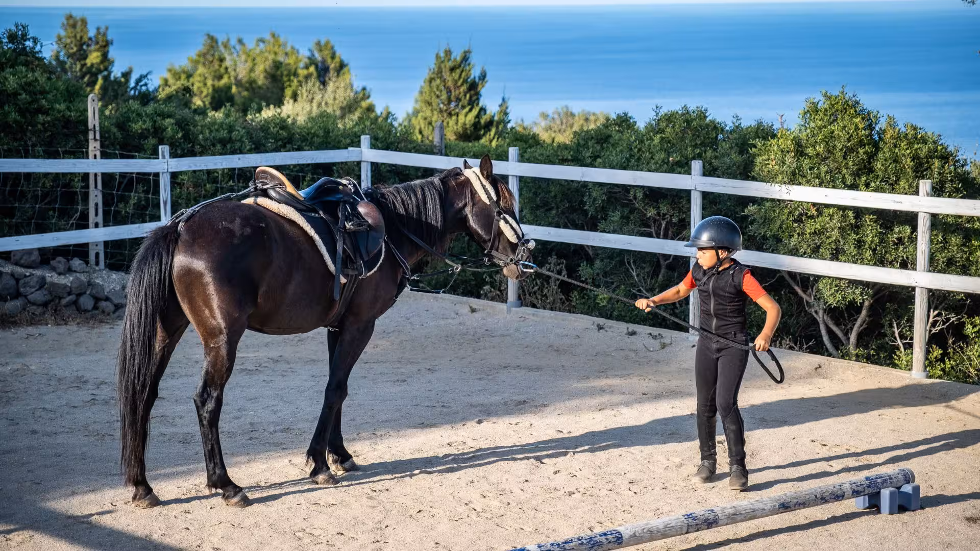 A young rider trains a horse in a Dorgali arena, with the Gulf of Orosei as a breathtaking backdrop.