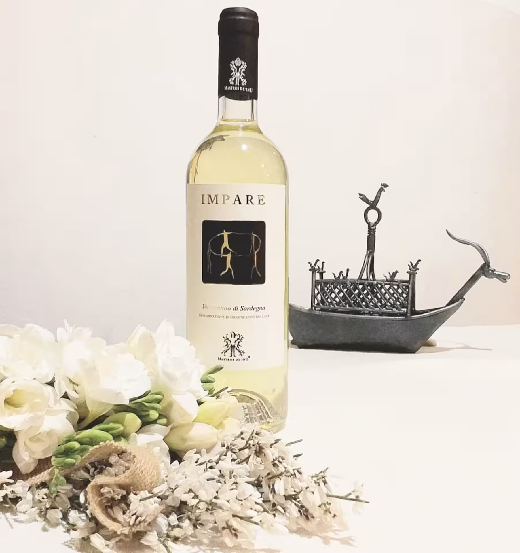 Impare white wine bottle surrounded by flowers and a decorative sculpture, showcasing Sardinian elegance for tasting tours.