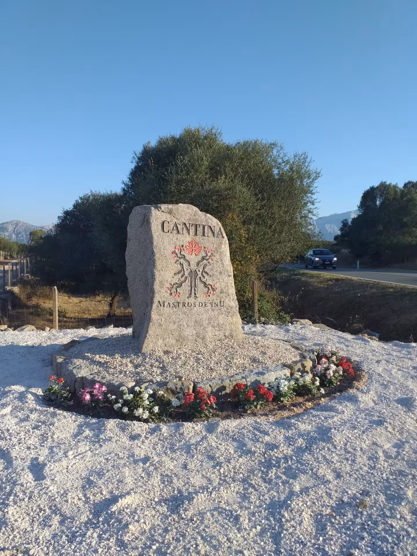 Entrance sign to a picturesque winery in Dorgali, surrounded by vibrant flowers and lush greenery.