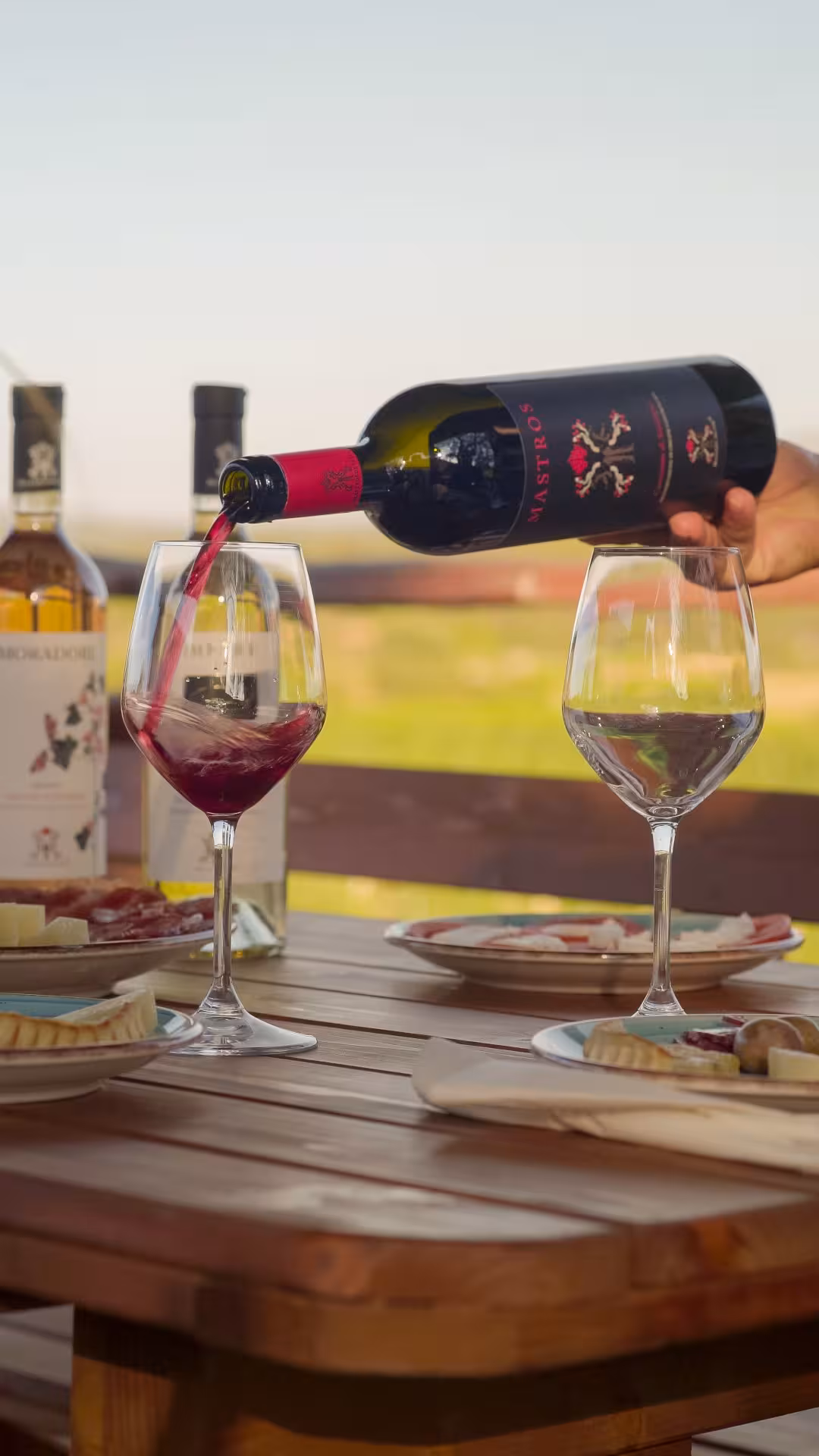 Red wine being poured into glasses beside cheese and charcuterie on a sunny Dorgali winery tour.