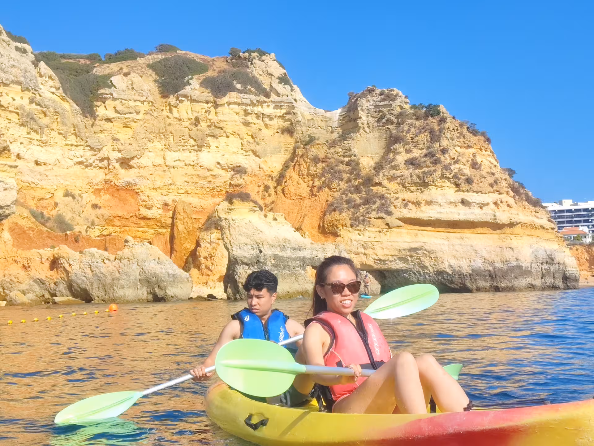 Smiling pair in a double kayak cruise past golden Algarve cliffs on a relaxing Portugal seaside excursion